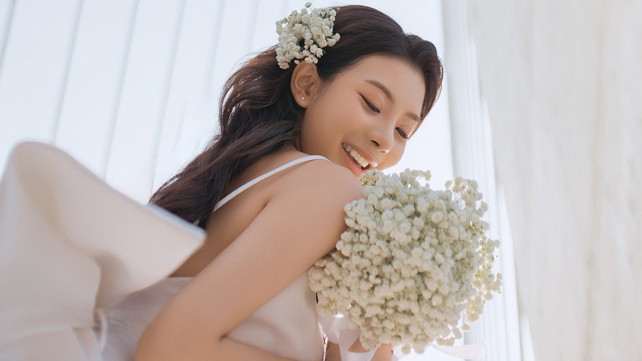 A képen egy japán nő mosolyog menyasszonyi ruhában, kezében virágcsokrot tart.