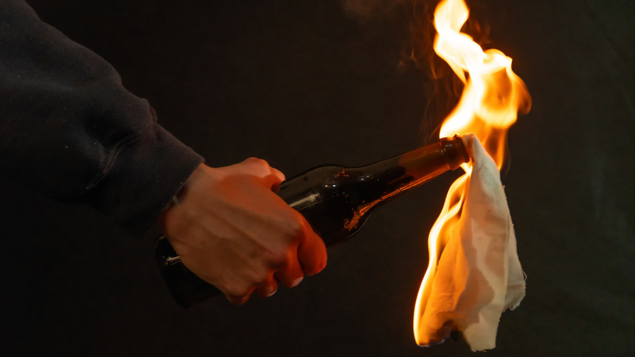 A hand holding a bottle with a burning rag against a dark background - symbolic of street protest or conflict