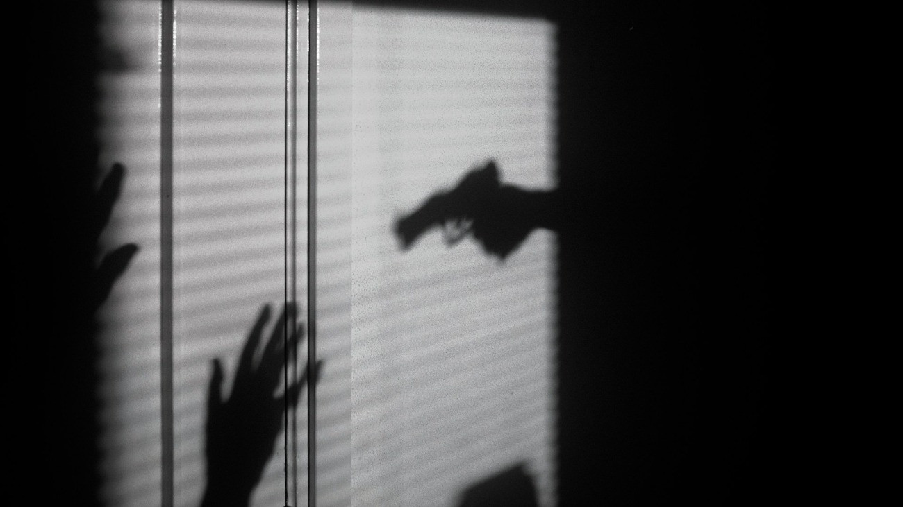 Egy pisztollyal elkövetett támadás árnyékai a falon.