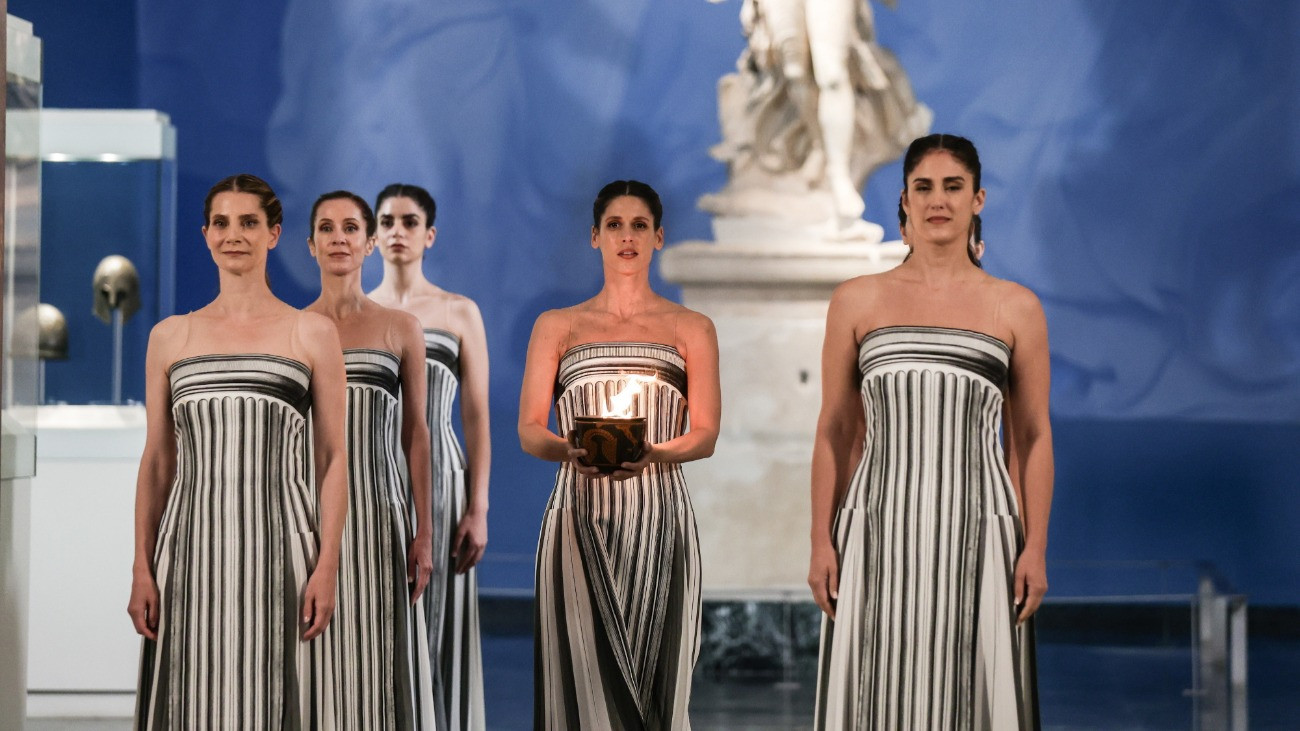 Olümpia, 2025. november 26. A fõpapnõ szerepét játszó Mary Mina görög színésznõ (k) a cserépedényben lévõ olimpiai lángot tartja a kezében a láng fellobbantási ünnepségén az eredeti olimpiai játékok helyszínén, az ókori Olümpia Régészeti Múzeumában 2025. november 26-án.  A 2026-os téli olimpiát február 6. és 22. között, a paralimpiát március 6. és 15. között rendezi Milánó és Cortina dAmpezzo közösen. ban 2024. április 16-án.