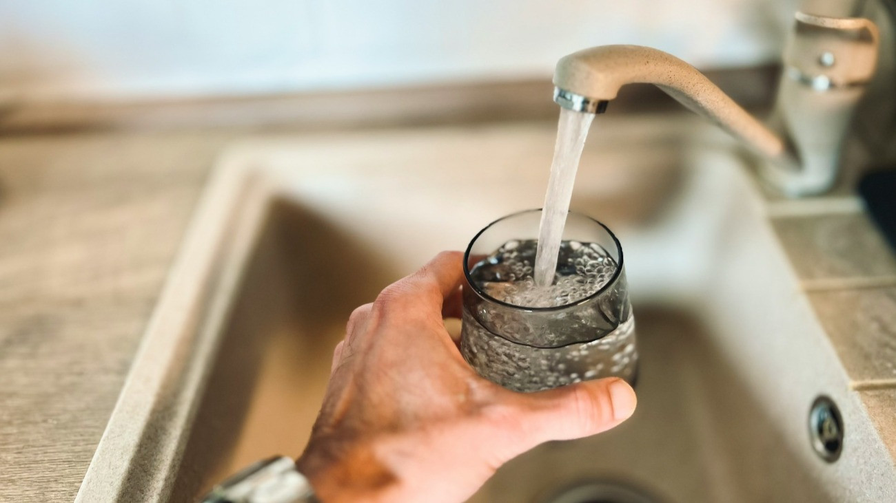 Egy szomjas férfi tölt magának egy pohár vizet a csapból.