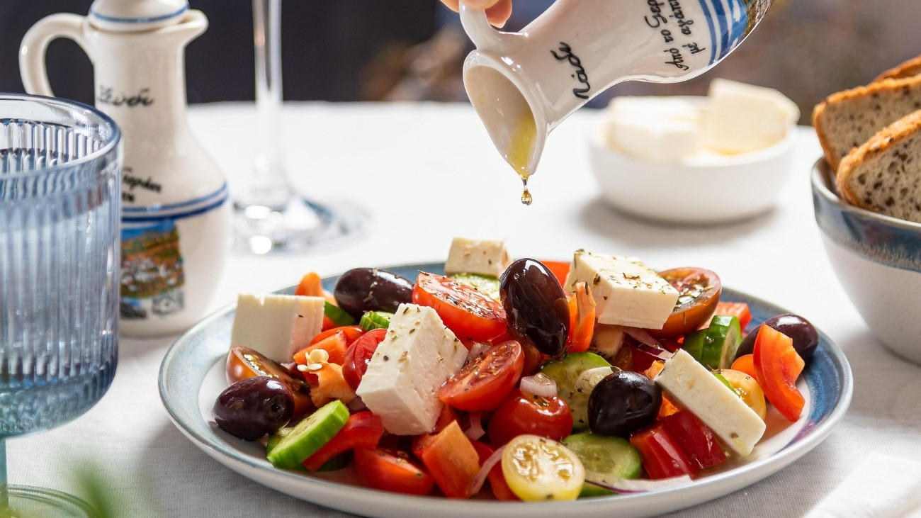 Görög salátára olívaolajat önt valaki.