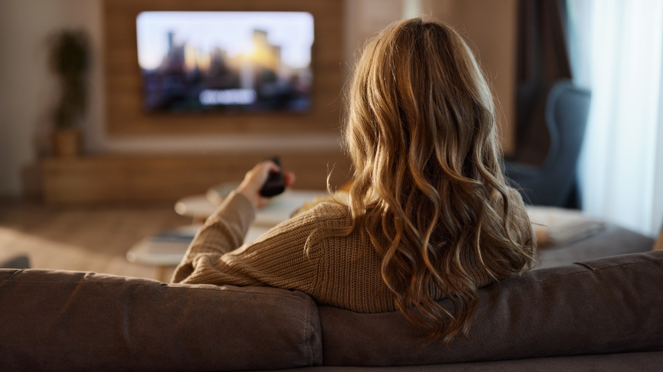 Kanapén pihenve tévézik egy hölgy a nappaliban.