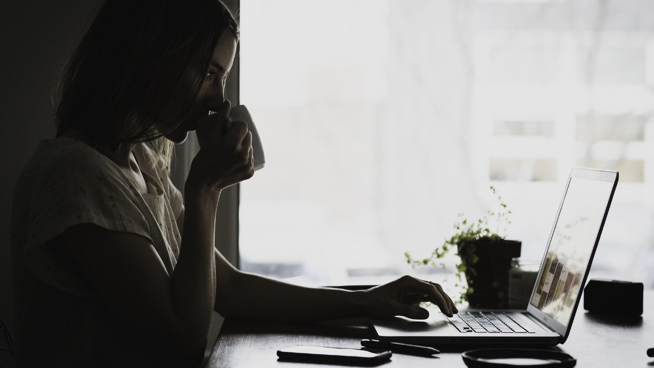 Egy fiatal nő félhomályban ül a laptop előtt.