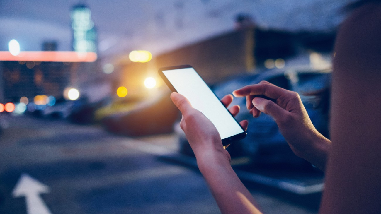 Egy nő okostelefonnal a kezében este az utcán.