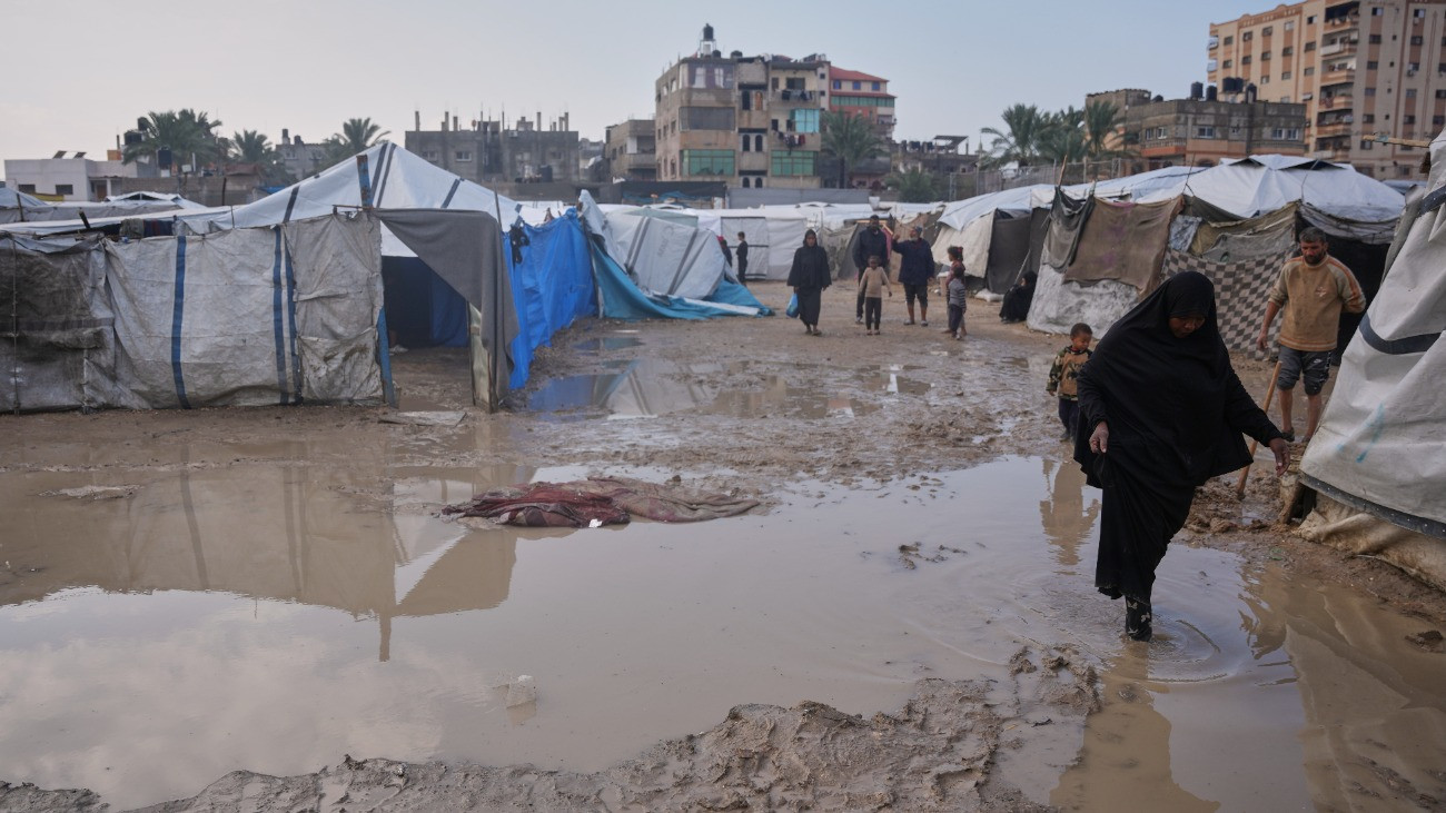 Sártengerben gyalogol árvízben álló lakósátrak mellett egy palesztin asszony a Hamász palesztin iszlamista szervezet és Izrael közötti háború miatt hajléktalanná vált palesztin emberek sátortáborában Gázai övezet középsõ részén fekvõ Deir al-Balahban 2025. december 12-én.