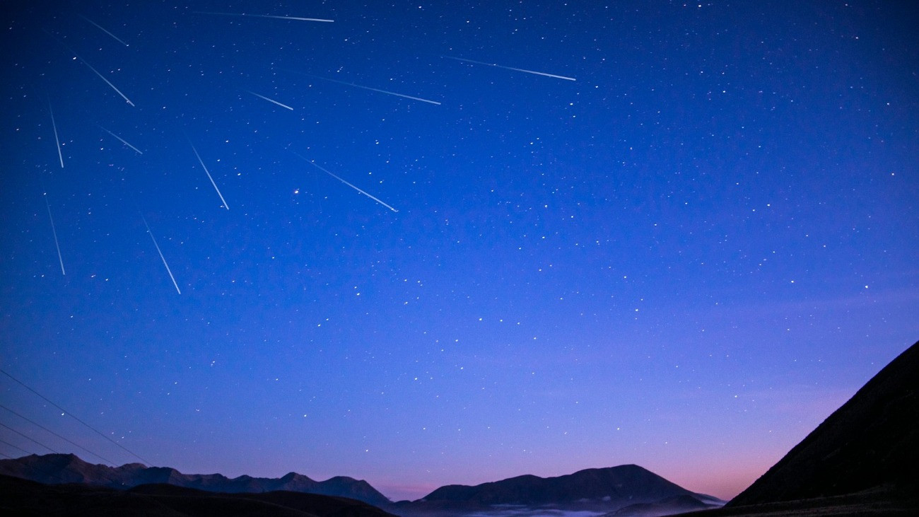 Hullócsillagok az éjszakai égbolton egy hegyvidékes táj fölött.