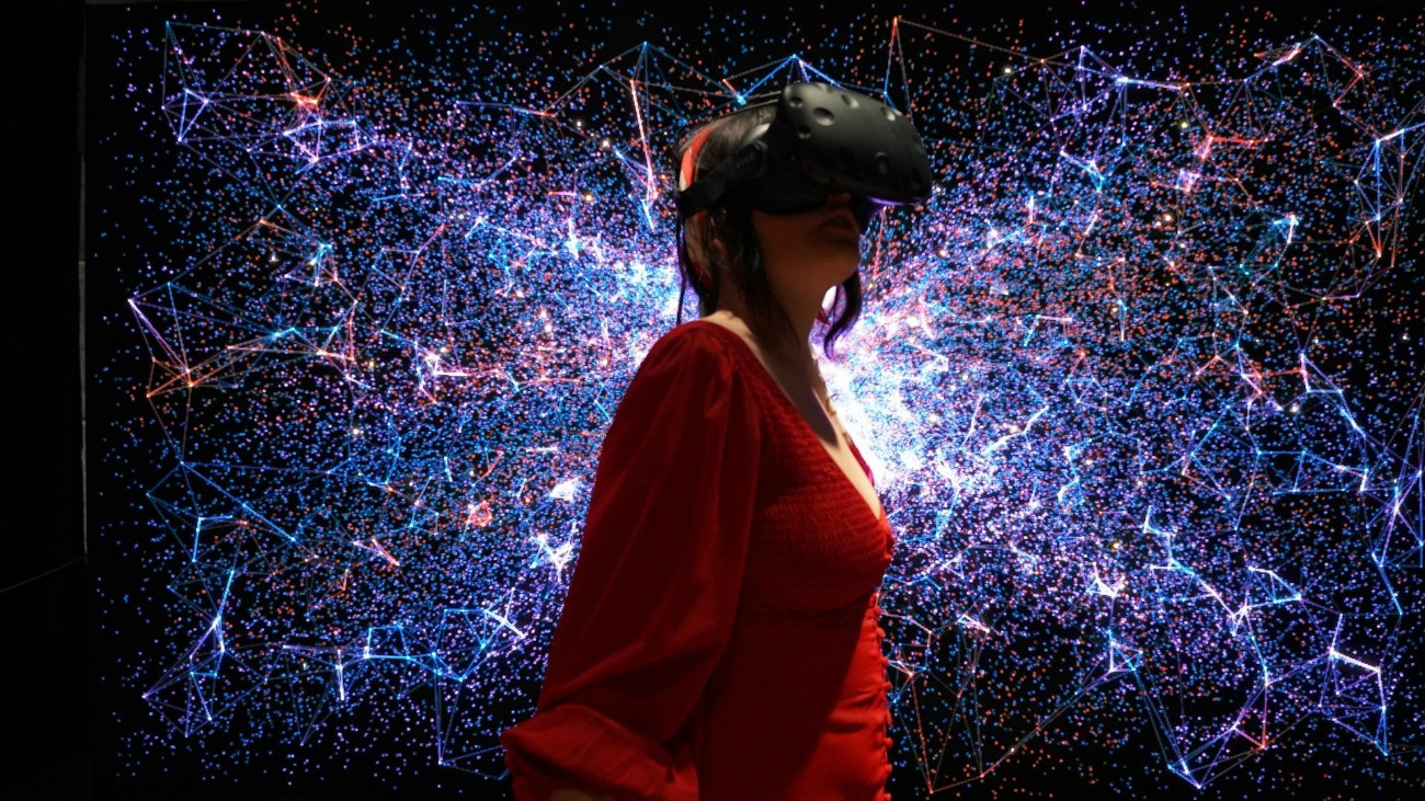 Egy fiatal nő VR-szemüvegben (virtuális valóság), színes, digitális háttér előtt.