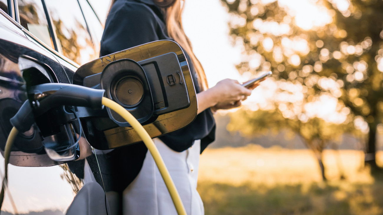Elektromos autót tölt egy fiatal nő.